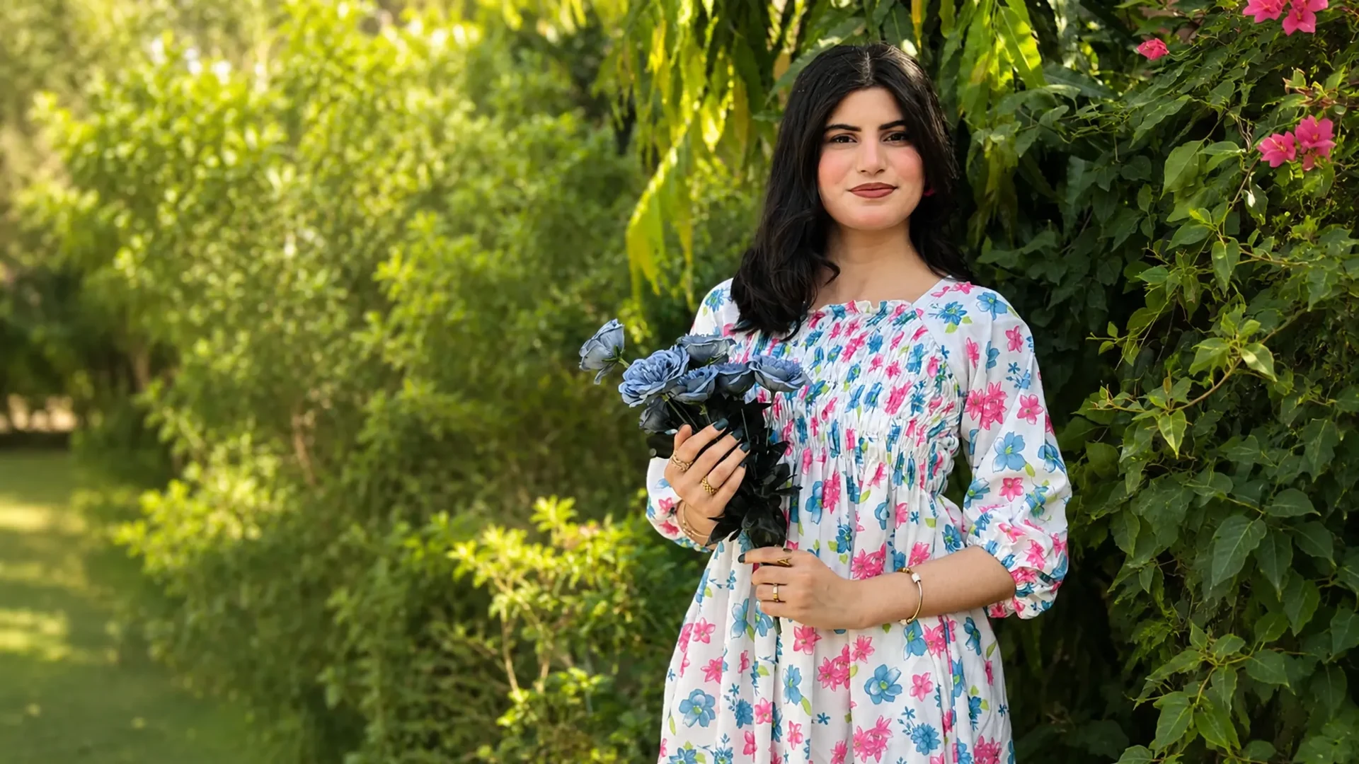 Woman wearing a white dress with pink and blue florals while holding blue flowers