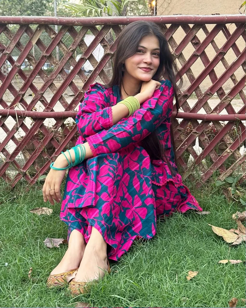 Woman seated outdoors wearing a vibrant pink and teal printed outfit