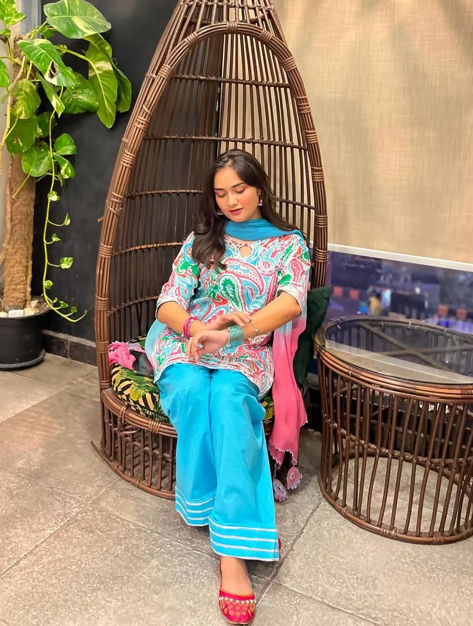 Woman seated in a colorful printed top with turquoise trousers